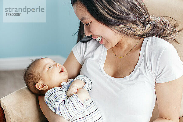 Asiatische Mutter hält schaukelnden neugeborenen Säugling Baby Sohn. Zuhause Lebensstil