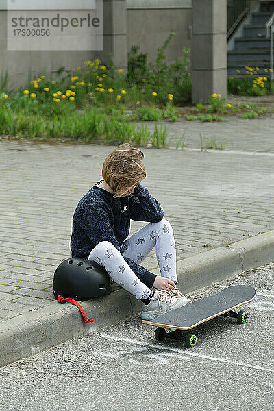 Ein müdes Kind sitzt neben einem Skateboard.