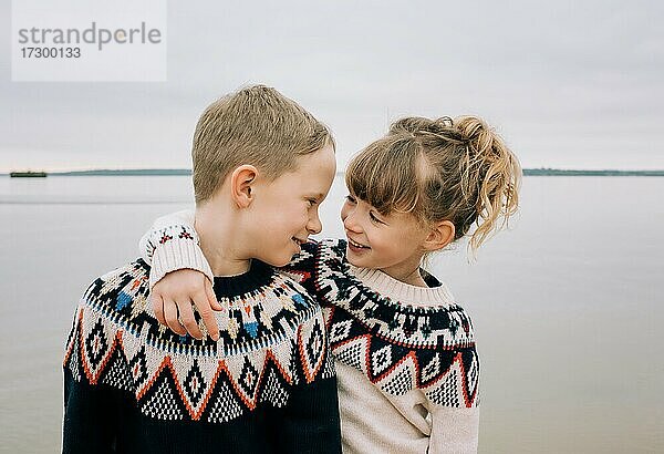 Bruder und Schwester umarmen und lächeln gemeinsam am Strand im Vereinigten Königreich