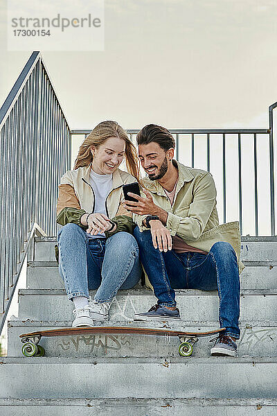 Junges gemischtrassiges Paar lächelt  während sie auf ein Telefon schauen