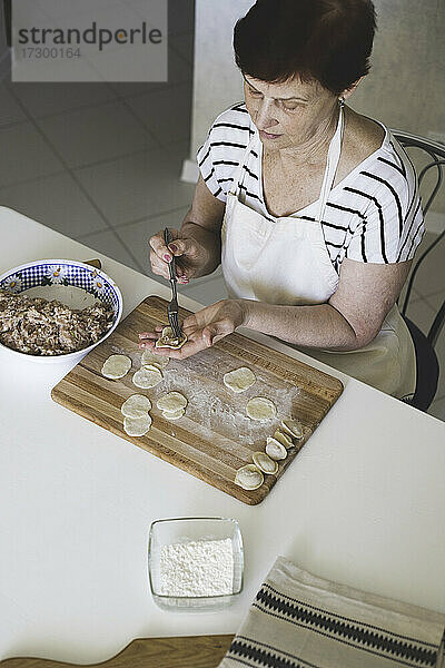 Eine Frau in einer weißen Küche bereitet traditionelle russische Knödel aus Fleisch und Teig zu