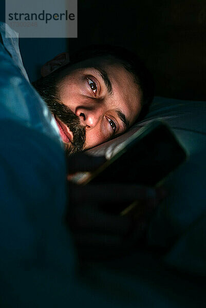 Junger Mann benutzt Smartphone im Bett