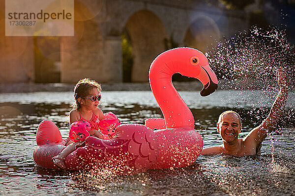 Vater und Tochter spielen im Fluss mit einem Flamingo-Schwimmkörper im Sommer