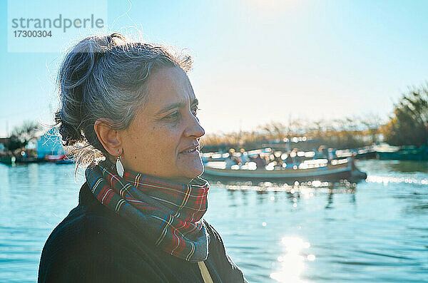 Porträt einer Frau mittleren Alters mit weißem Haar  die auf die Boote schaut  im Gegenlicht