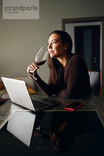Brünette Frau trinkt Wein und benutzt einen Laptop