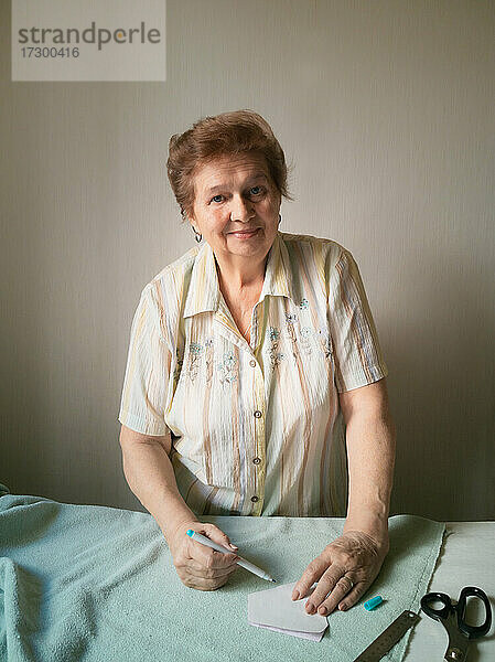 Eine ältere Frau fertigt ein Muster für eine medizinische Maske auf einem Stoff an