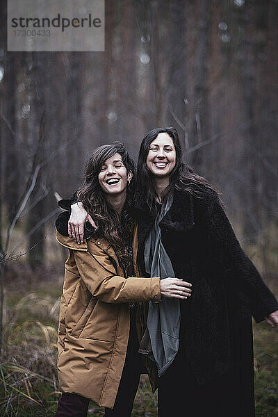 Freundinnen lachen und umarmen sich im Freien in einem Kiefernwald in Deutschland