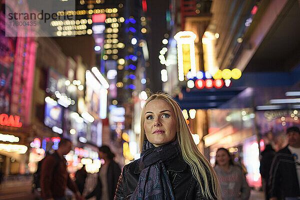 Erwachsene Frau auf leuchtender Stadtstraße am Abend