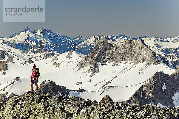 Junge attraktive Rucksacktouristin steht auf einem felsigen Grat mit Bergblick