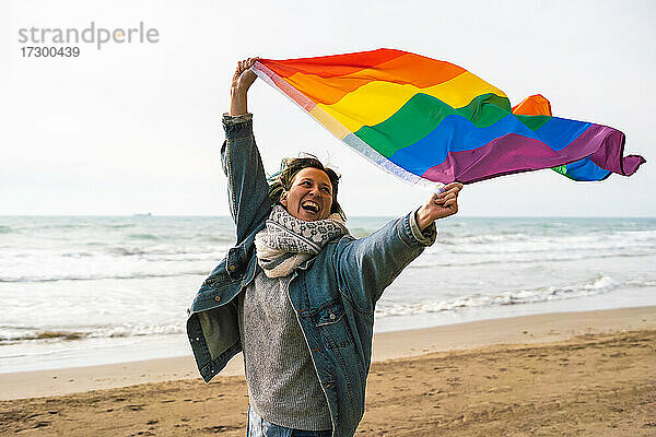 Frau läuft mit bunter LGBT-Flagge  die am Strand weht