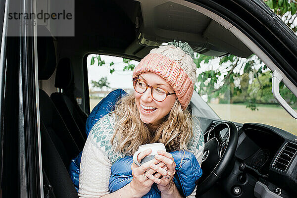 eine Frau  die in ihrem Wohnmobil sitzt und fröhlich lacht  während sie Kaffee trinkt