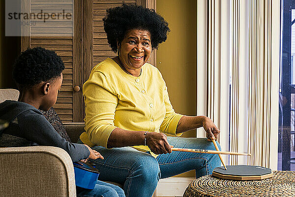 Fröhliche ältere Frau spielt Schlagzeug  während ihr Enkel zu Hause Gitarre übt