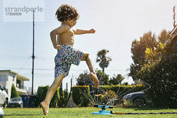 Shirtless Junge springt über Sprinkler im Hinterhof gegen den Himmel