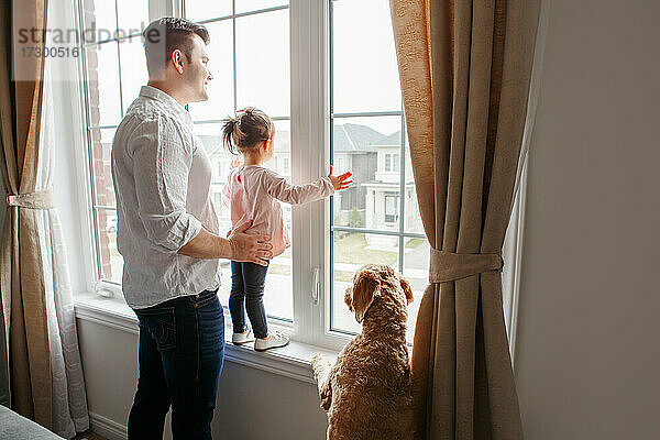 Vater Vater mit Kleinkind Mädchen und Hund Haustier Blick aus dem Fenster zu Hause