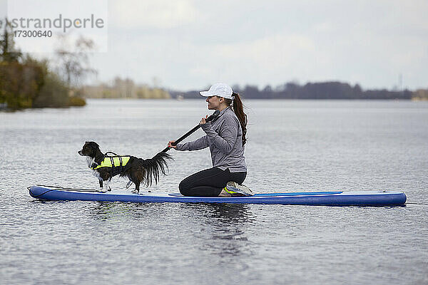 Eine Frau paddelt mit einem kleinen Hund auf einem See.