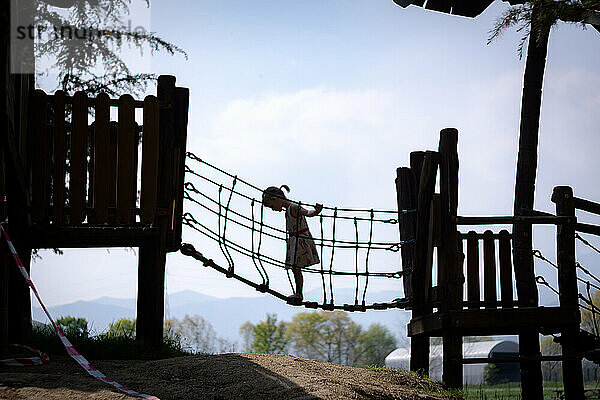 Silhouette junges Mädchen steht auf Kinderseilbrücke auf Spielplatz