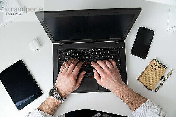 Mann arbeitet zu Hause an einem Laptop auf einem weißen Schreibtisch  Draufsicht