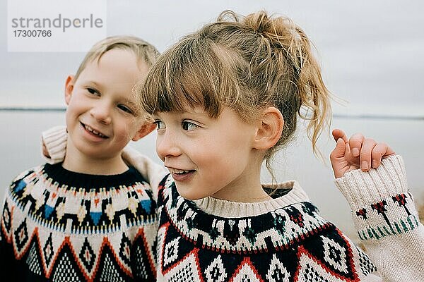 Bruder und Schwester spielen und umarmen sich im Herbst am Strand