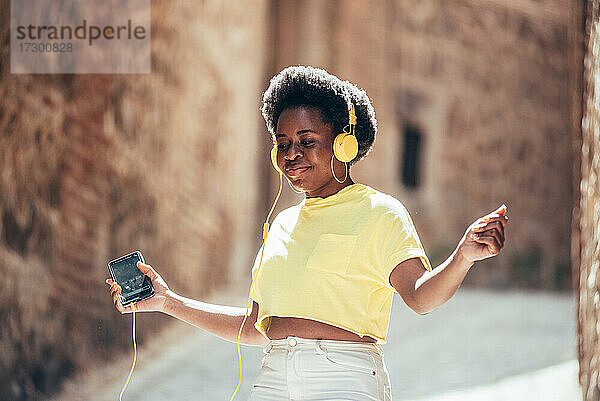 Porträt eines schwarzen Mädchens mit Afro-Haar  das in einer Altstadtstraße Musik hört und tanzt.