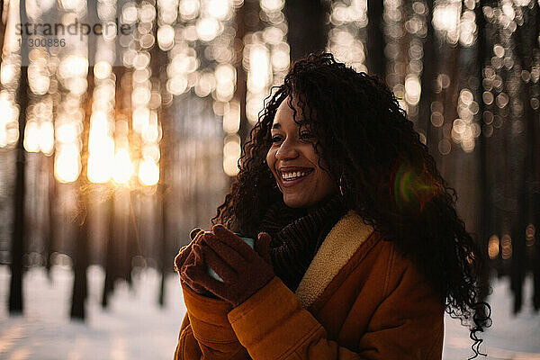 Glückliche junge Frau mit einer Tasse Tee in einem Park im Winter
