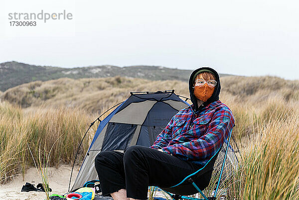 Person im Campingstuhl sitzend mit Maske an einem bedeckten Tag am Strand