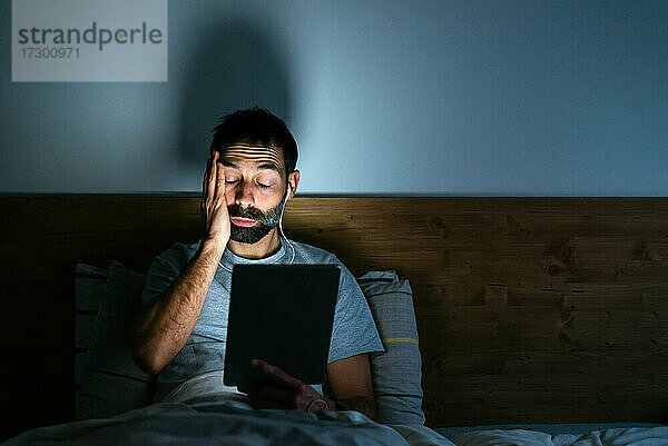 Müder junger Mann wischt sich bei der Arbeit am Tablet die Augen