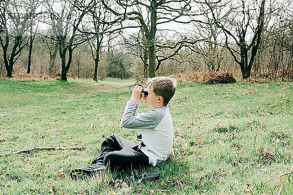 Junge  der durch ein Fernglas die Natur in der englischen Landschaft beobachtet