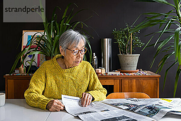 Ältere Frau im gelben Pullover liest zu Hause Zeitung