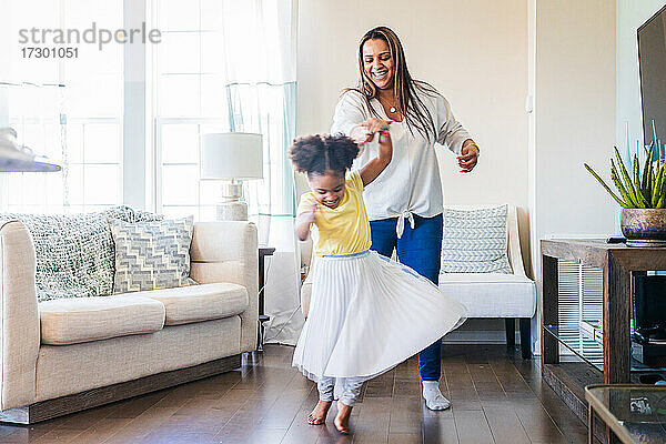 Glückliche Mutter hält die Hand ihrer Tochter  die im Wohnzimmer zu Hause Tanz übt