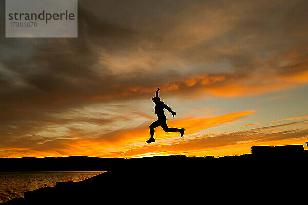 Silhouette eines springenden Mannes mit Mütze im Sonnenuntergang