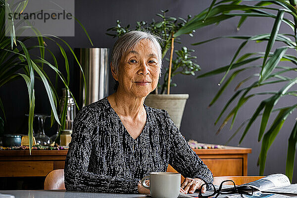 Porträt der lächelnden asiatischen Senior Frau sitzt am Tisch zu Hause