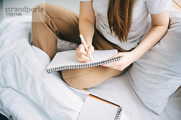 Mädchen schreibt in ein Notizbuch und hört Musik im Bett