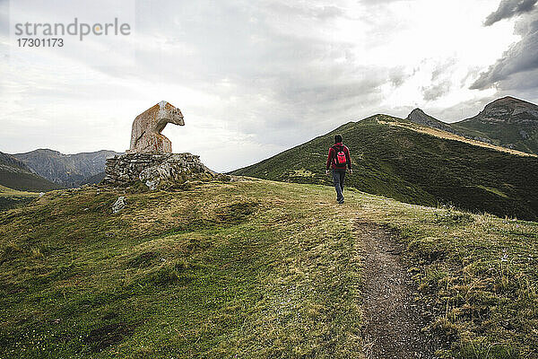 Mann  der in den Bergen neben der Bärenstatue Picos de Europa spazieren geht