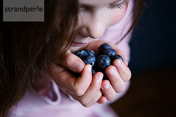 Lächelndes Mädchen pflückt frische Blaubeeren auf dunklem Hintergrund