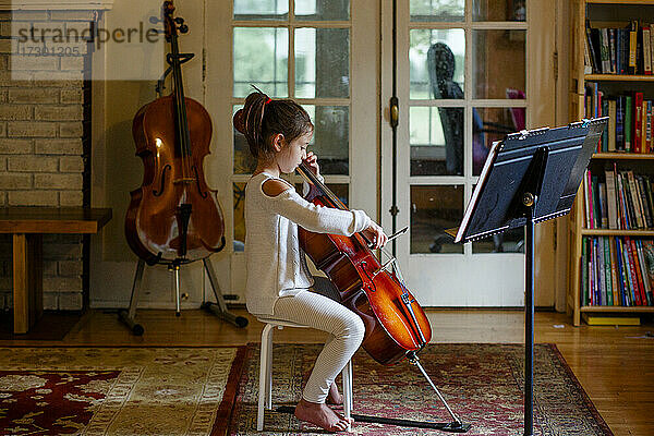 ein konzentriertes  anmutiges Kind übt zu Hause im Fensterlicht Cello