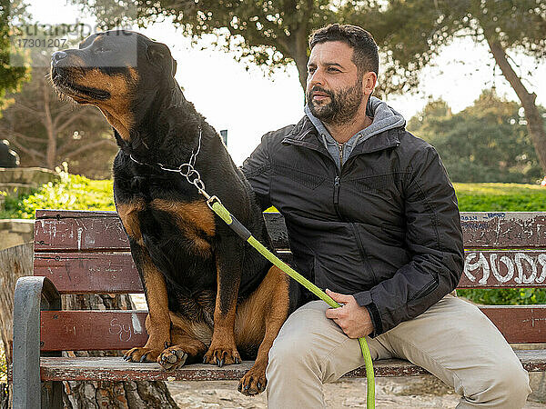 Mann sitzt auf einer Parkbank neben seinem Rottweiler-Hund