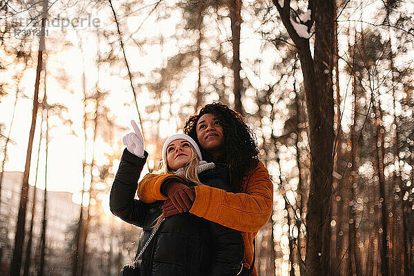 Junge Frau umarmt ihre Freundin stehend im Park im Winter