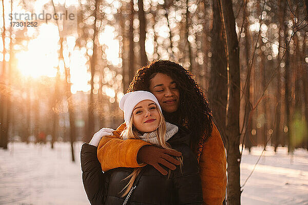 Glückliche junge Frau umarmt ihre Freundin im Park stehend im Winter