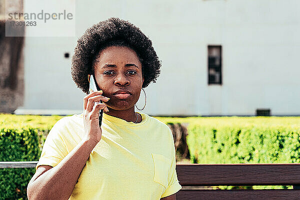 Porträt eines schwarzen Mädchens mit Afro-Haar und Ohrringen  das in einer städtischen Umgebung telefoniert.