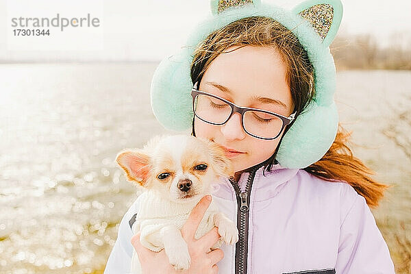 Porträt eines glücklichen Teenager-Mädchens mit ihrem kleinen Chihuahua-Hund. Ein Mädchen auf dem Hintergrund der Natur umarmt ihren Chihuahua-Hund in der Kleidung.