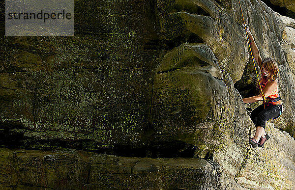 Frau klettert auf den Sandsteinfelsen am Harrison's Rock in England