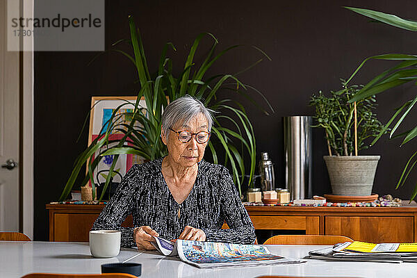 Ältere Frau liest Zeitung und sitzt mit Kaffee am Tisch