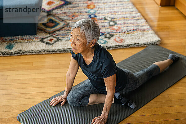 Ältere asiatische Frau dehnt sich auf einer Übungsmatte im Wohnzimmer