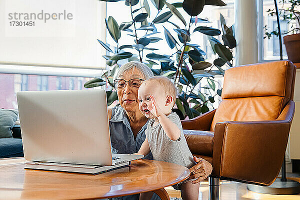 Ältere Frau sitzt mit ihrer Enkelin zusammen und benutzt einen Laptop für einen Videoanruf