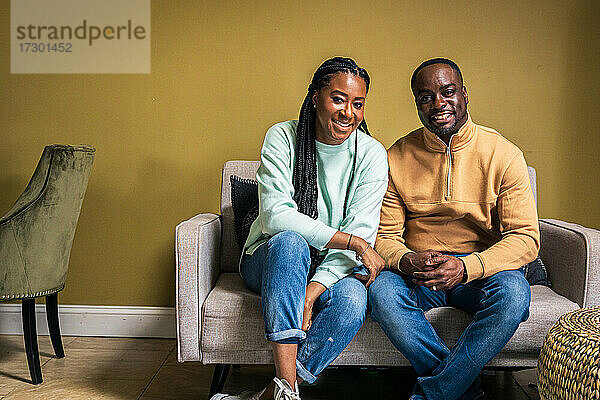 Porträt eines lächelnden reifen Paares  das zu Hause auf dem Sofa sitzt