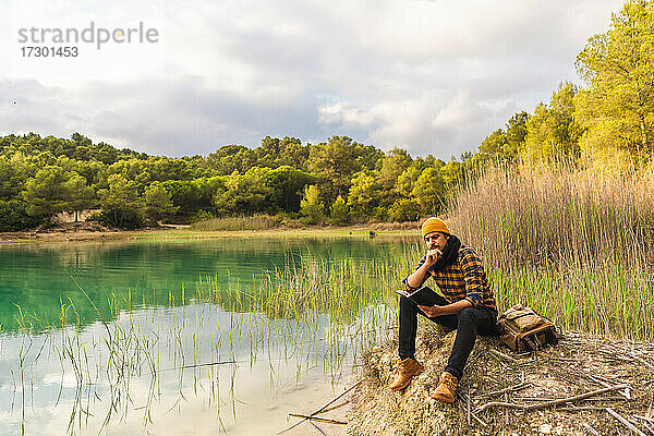 Spanischer Reisender  der an einem ruhigen See sitzend ein Buch liest
