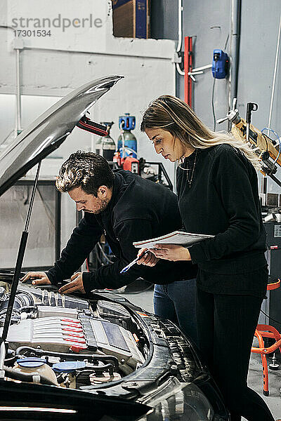 Männlicher Mechaniker bringt weiblichen Mechanikern bei  wie man ein Fahrzeug repariert