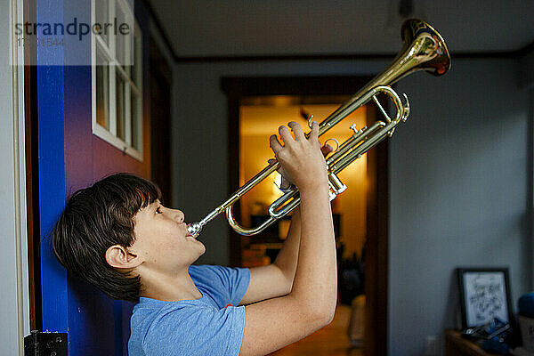 Ein Junge steht in einer bunten offenen Tür und spielt Trompete