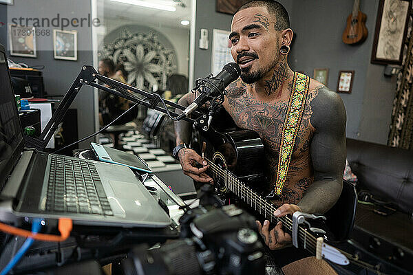 Asiatischer Mann spielt Gitarre im Studio und singt