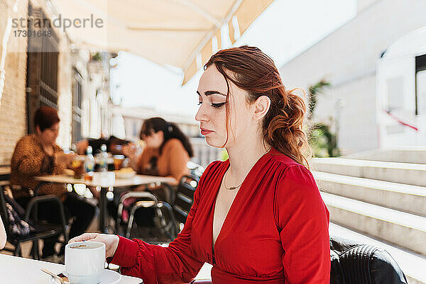 Junge rothaarige Frau in roter Bluse bei einem Kaffee auf einer Terrasse